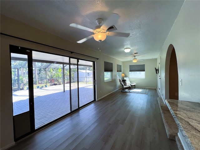 empty room with ceiling fan, dark wood-type flooring, a healthy amount of sunlight, and a textured ceiling