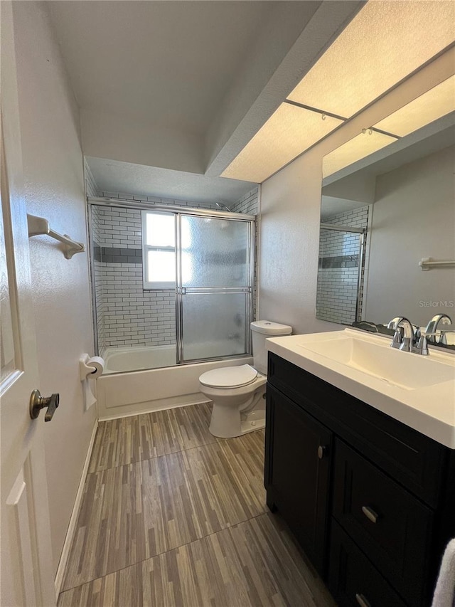 full bathroom with shower / bath combination with glass door, hardwood / wood-style floors, vanity, and toilet