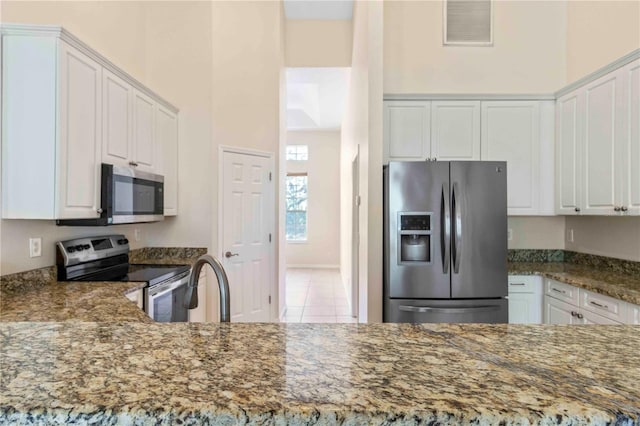 kitchen with dark stone countertops, white cabinetry, light tile patterned floors, and stainless steel appliances