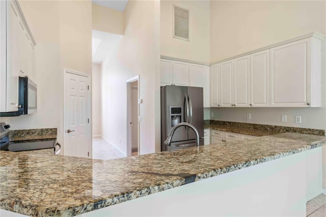 kitchen featuring dark stone counters, white cabinets, a towering ceiling, kitchen peninsula, and stainless steel appliances