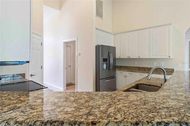 kitchen with dark stone counters, white cabinets, sink, a towering ceiling, and stainless steel fridge with ice dispenser