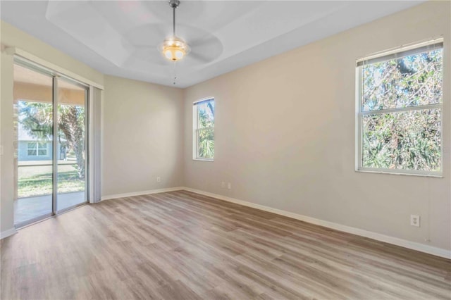 unfurnished room featuring a tray ceiling, ceiling fan, and light hardwood / wood-style floors