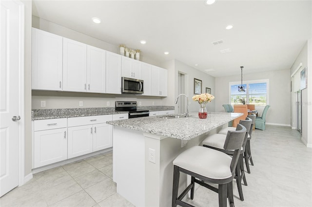 kitchen featuring stainless steel appliances, white cabinetry, a center island with sink, and sink