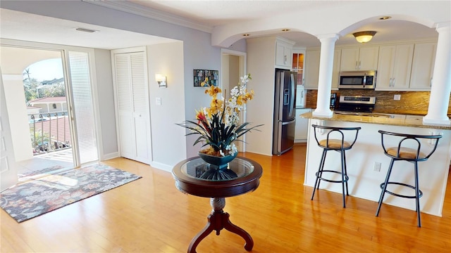 kitchen featuring ornate columns, white cabinetry, stainless steel appliances, and light wood-type flooring