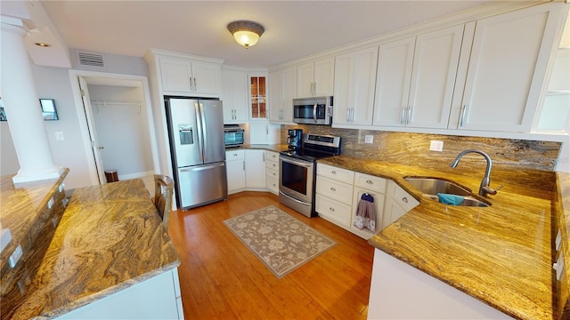 kitchen featuring light wood-type flooring, dark stone counters, stainless steel appliances, sink, and white cabinetry