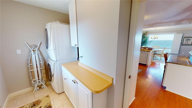 laundry room with a chandelier, cabinets, stacked washer and dryer, and light hardwood / wood-style flooring