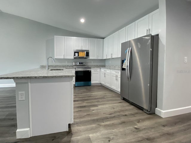 kitchen with white cabinets, sink, vaulted ceiling, appliances with stainless steel finishes, and light stone counters