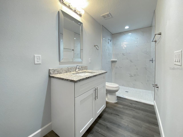 bathroom featuring vanity, a textured ceiling, tiled shower, wood-type flooring, and toilet