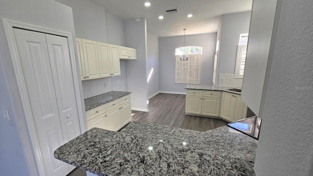 kitchen with decorative light fixtures, kitchen peninsula, dark wood-type flooring, and dark stone counters