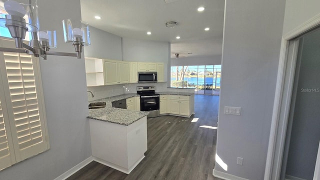 kitchen with white cabinets, dark hardwood / wood-style floors, dark stone countertops, kitchen peninsula, and stainless steel appliances