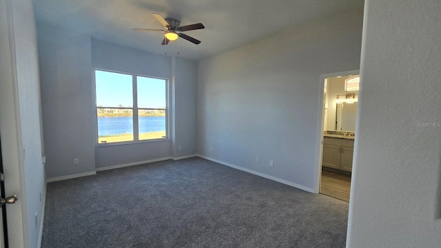 spare room with ceiling fan, a water view, and dark carpet