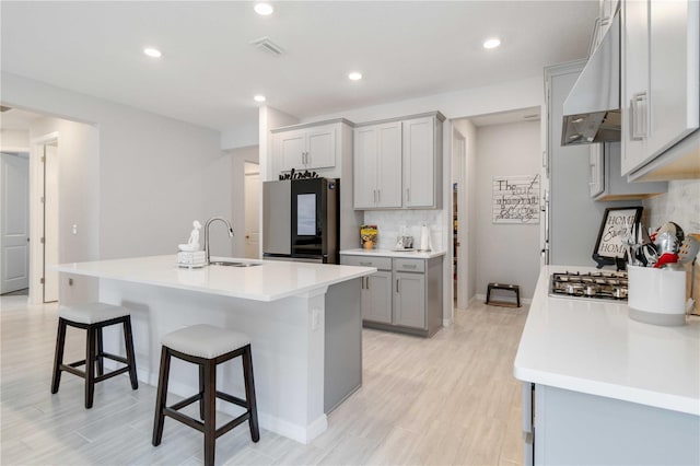 kitchen featuring stainless steel refrigerator, sink, a kitchen breakfast bar, decorative backsplash, and a kitchen island with sink