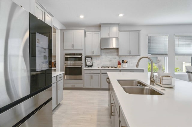 kitchen with sink, tasteful backsplash, gray cabinets, exhaust hood, and appliances with stainless steel finishes