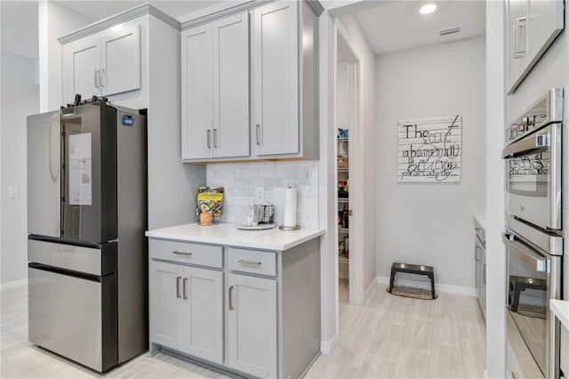 kitchen featuring gray cabinets, decorative backsplash, light hardwood / wood-style flooring, and appliances with stainless steel finishes