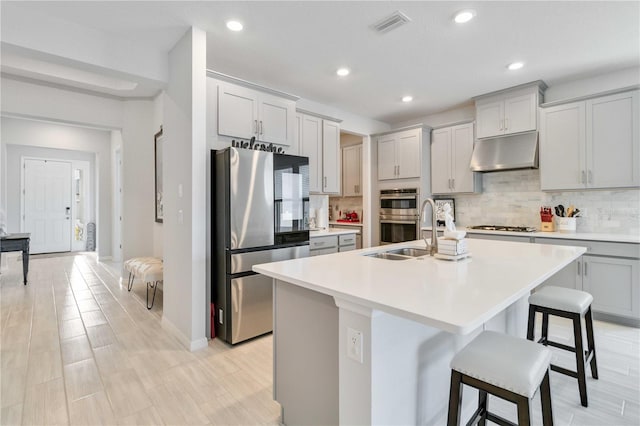 kitchen featuring decorative backsplash, appliances with stainless steel finishes, a kitchen breakfast bar, sink, and an island with sink