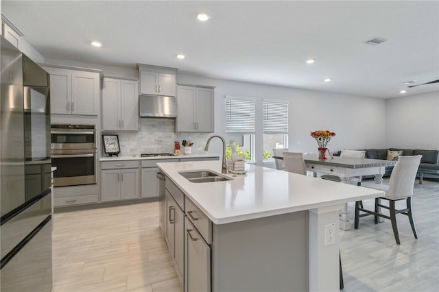 kitchen featuring sink, a kitchen island with sink, gray cabinetry, and exhaust hood