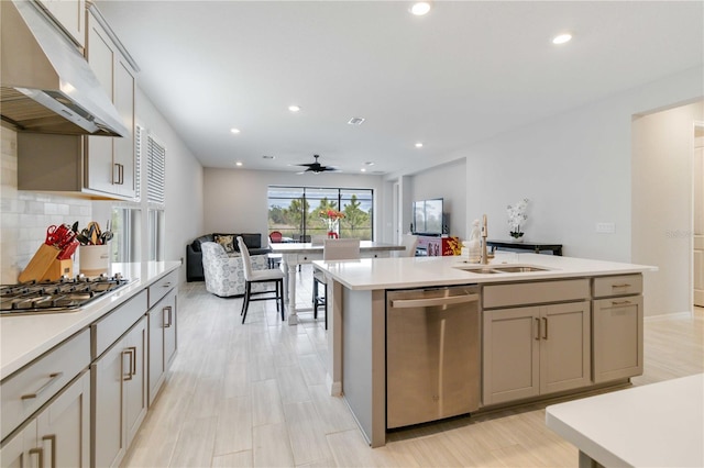 kitchen with ceiling fan, sink, stainless steel appliances, decorative backsplash, and a center island with sink