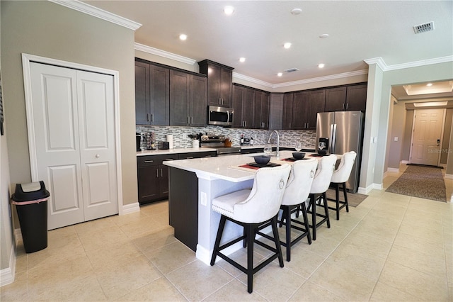 kitchen featuring a kitchen bar, appliances with stainless steel finishes, dark brown cabinets, a kitchen island with sink, and light tile patterned floors