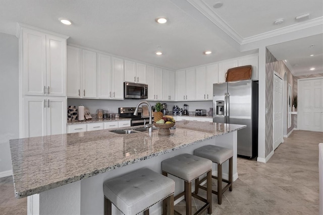 kitchen featuring a breakfast bar, stainless steel appliances, a kitchen island with sink, sink, and white cabinets