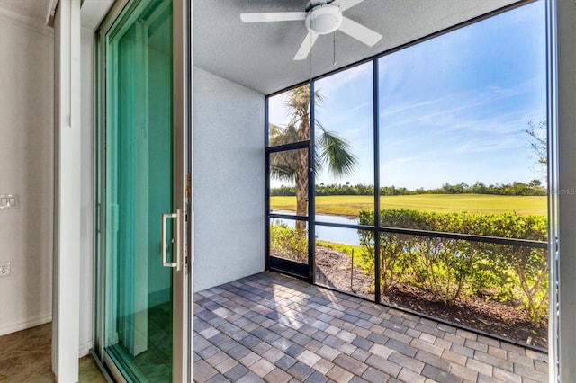 unfurnished sunroom featuring ceiling fan and a water view