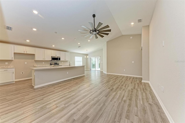 kitchen with appliances with stainless steel finishes, vaulted ceiling, a kitchen island with sink, light hardwood / wood-style flooring, and white cabinets