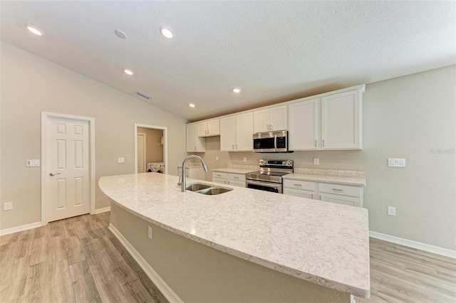 kitchen with white cabinets, sink, an island with sink, appliances with stainless steel finishes, and light hardwood / wood-style floors