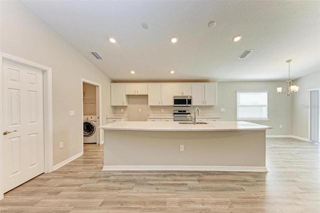 kitchen featuring a kitchen island with sink, appliances with stainless steel finishes, light hardwood / wood-style floors, white cabinetry, and washer / clothes dryer