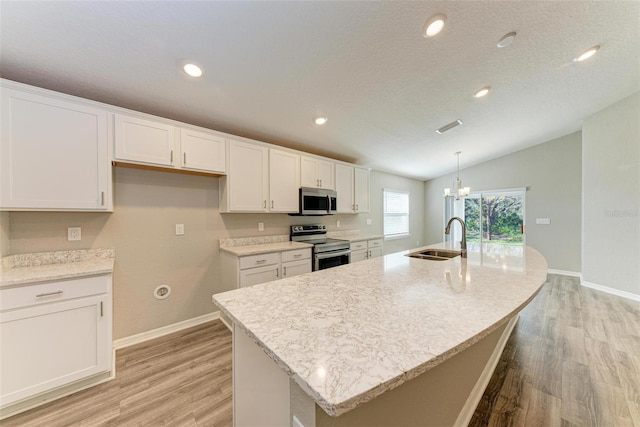 kitchen with a center island with sink, white cabinetry, lofted ceiling, and appliances with stainless steel finishes