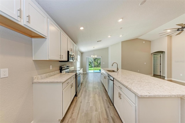 kitchen with appliances with stainless steel finishes, vaulted ceiling, sink, a center island with sink, and white cabinets