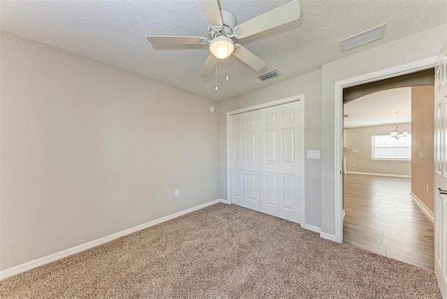 unfurnished bedroom featuring a textured ceiling, a closet, carpet, and ceiling fan with notable chandelier