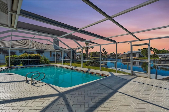 pool at dusk featuring glass enclosure, a patio area, and a water view