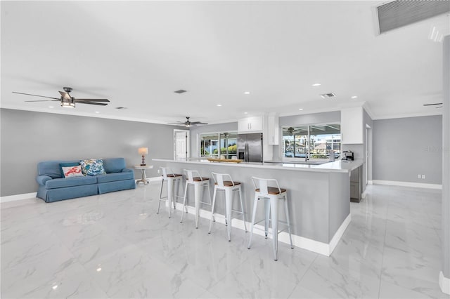 kitchen with a kitchen bar, stainless steel fridge, kitchen peninsula, ceiling fan, and white cabinets