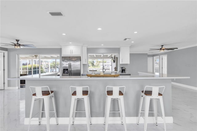 kitchen with white cabinetry, a large island, stainless steel fridge, a breakfast bar area, and ornamental molding