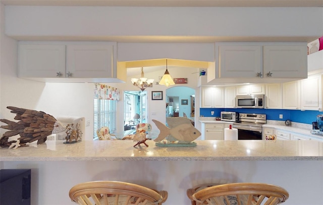 kitchen with kitchen peninsula, appliances with stainless steel finishes, a breakfast bar, an inviting chandelier, and white cabinetry