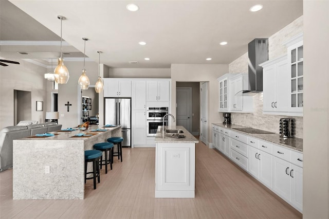 kitchen featuring a spacious island, wall chimney exhaust hood, decorative light fixtures, white cabinetry, and stainless steel appliances