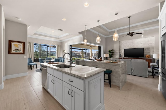 kitchen featuring light stone countertops, a raised ceiling, sink, a center island with sink, and white cabinets