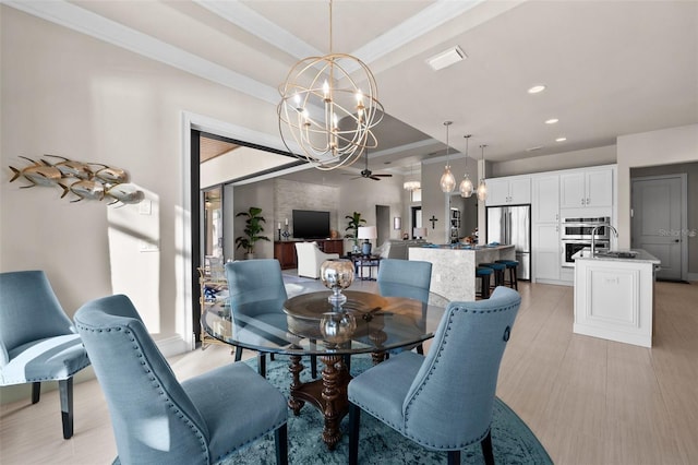 dining space featuring sink, a raised ceiling, light hardwood / wood-style flooring, ceiling fan with notable chandelier, and ornamental molding