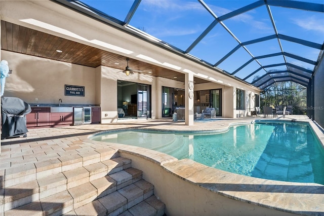 view of pool with glass enclosure, a patio area, sink, ceiling fan, and area for grilling