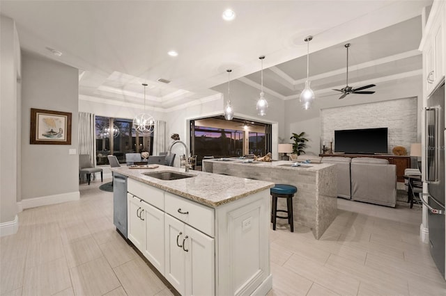 kitchen featuring a kitchen island with sink, sink, light stone countertops, a tray ceiling, and white cabinetry