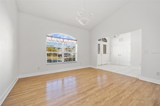 spare room with a notable chandelier, light wood-type flooring, and high vaulted ceiling