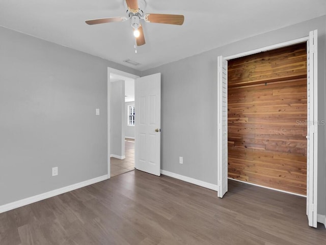 unfurnished bedroom featuring wooden walls, a closet, ceiling fan, and dark wood-type flooring