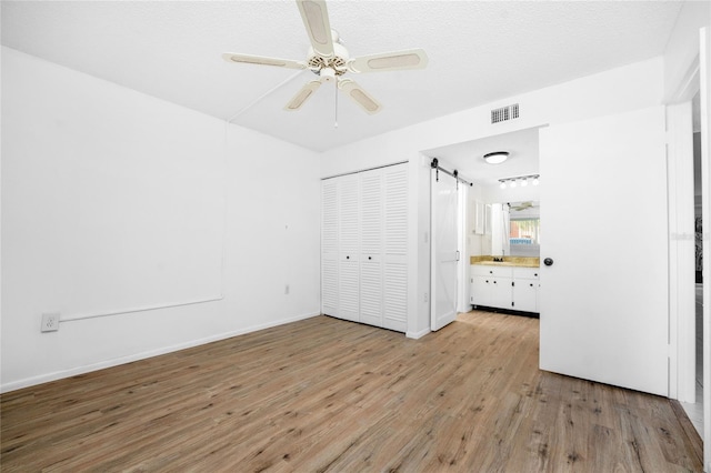 unfurnished bedroom with ensuite bath, light hardwood / wood-style floors, a textured ceiling, a barn door, and a closet