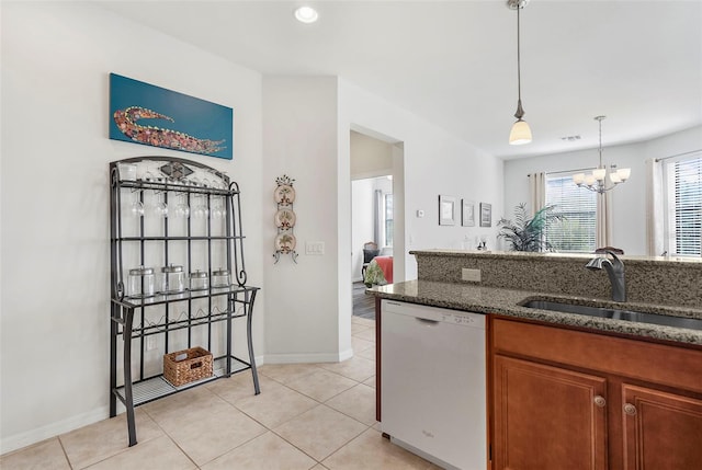 kitchen featuring dark stone counters, white dishwasher, sink, a chandelier, and hanging light fixtures