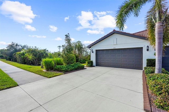 view of front facade with a tile roof, concrete driveway, a garage, and stucco siding