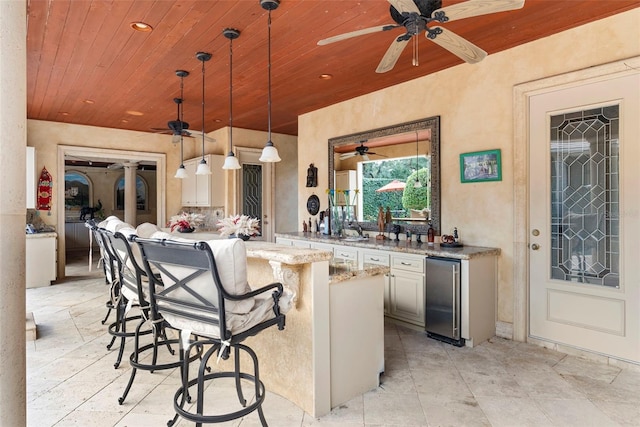 kitchen with light stone counters, wooden ceiling, hanging light fixtures, and a breakfast bar area