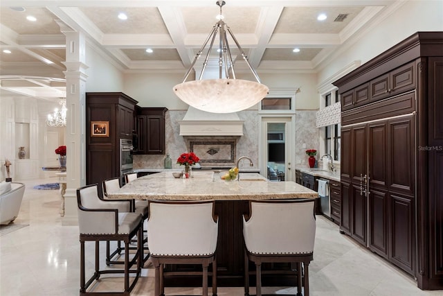 kitchen featuring coffered ceiling, a large island with sink, beam ceiling, decorative light fixtures, and a breakfast bar area