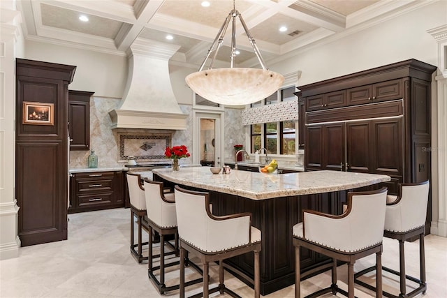 kitchen featuring premium range hood, a large island with sink, beam ceiling, and coffered ceiling