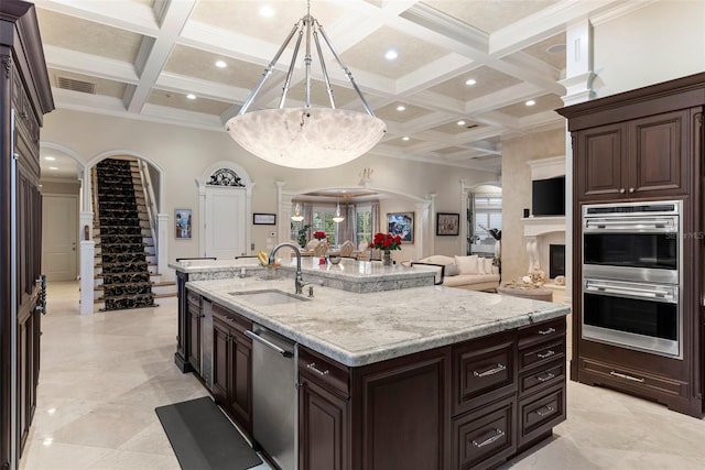 kitchen with coffered ceiling, a center island with sink, sink, appliances with stainless steel finishes, and decorative light fixtures