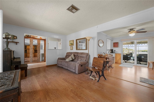 living room with ceiling fan, light wood-type flooring, and a textured ceiling