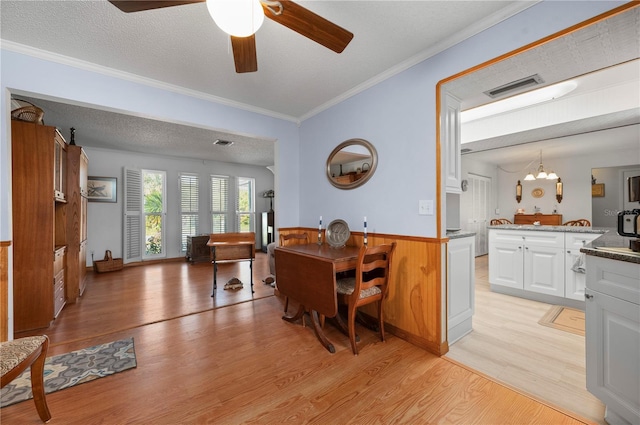 dining area with wood walls, light hardwood / wood-style floors, a textured ceiling, ceiling fan with notable chandelier, and ornamental molding